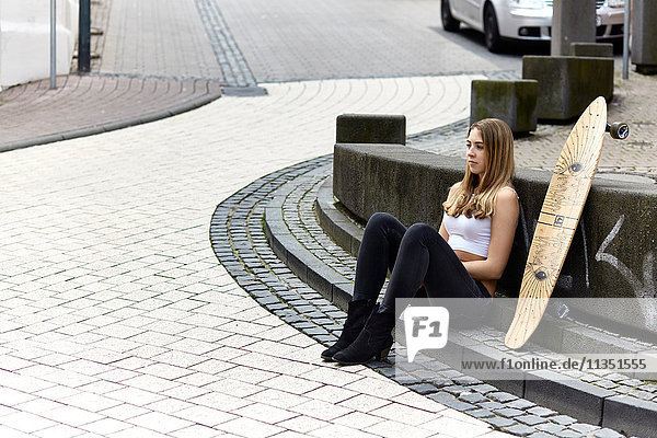 Sitzende junge Frau mit Skateboard