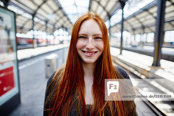 Portrait einer lächelnden rothaarigen jungen Frau auf dem Bahnsteig