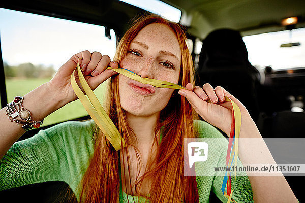 Playful young woman holding paper streamer in car