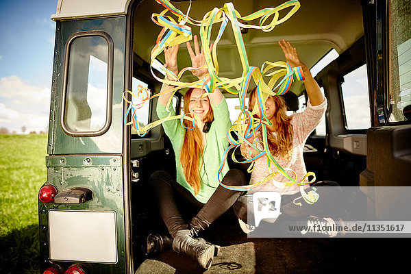 Two young women throwing paper streamers out of car