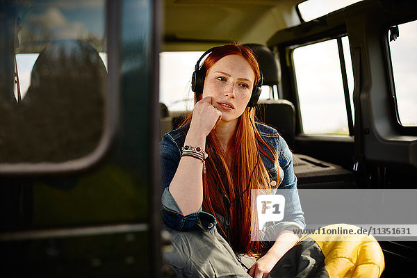 Young woman with sleeping bag and headphones in off-road vehicle