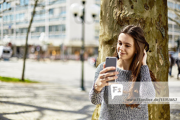Lächelnde Teenagerin mit Handy an einem Baum