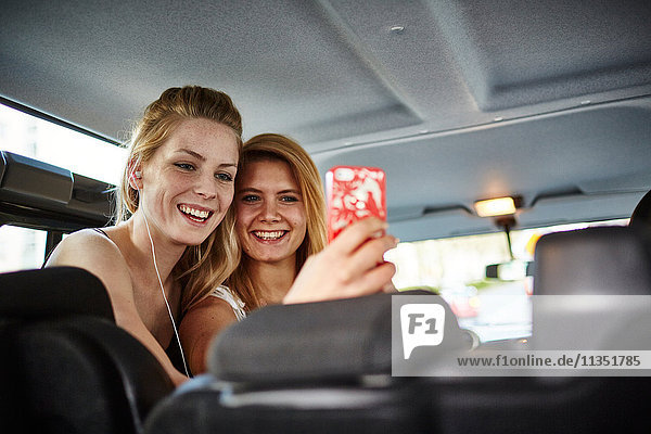 Zwei fröhliche junge Frauen im Auto machen ein Selfie