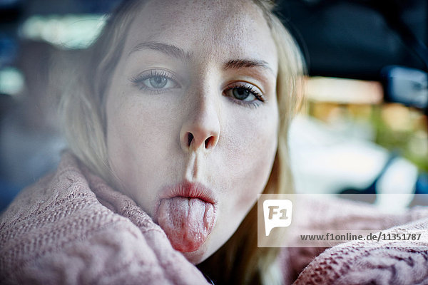 Young woman inside car sticking out tongue