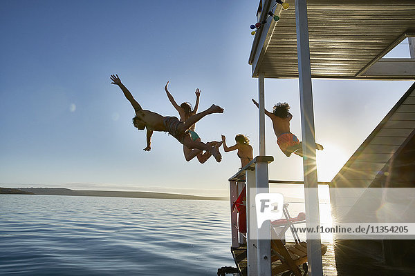 Junge erwachsene Freunde beim Sprung vom Sommerhausboot ins sonnige Meer