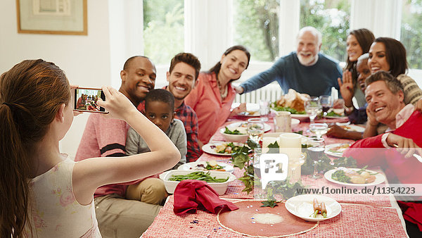 Girl with camera phone photographing multi-ethnic family at Christmas dinner table