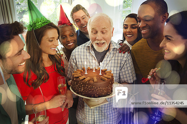 Multi-ethnische Familie beobachtet Senior Mann blasen Geburtstag Kerzen auf Schokolade Kuchen