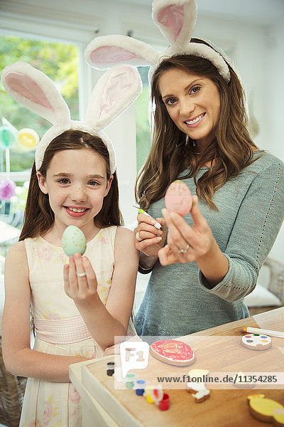 Portrait smiling mother and daughter wearing costume rabbit ears showing decorated Easter eggs