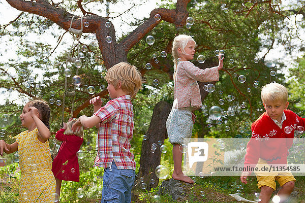 Group of young friends playing outdoors  reaching for bubbles