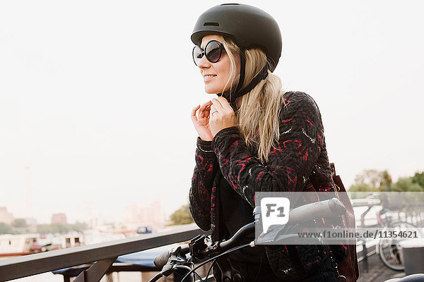 Junge Frau im Freien  Helm aufsetzen  bereit zum Fahrradfahren