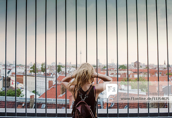 Young woman looking through railings  at view across rooftops  rear view
