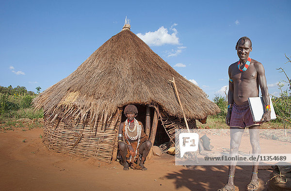 Mann des Karo-Stammes mit Laptop  während seine Frau in einer Hütte zusieht  Omo Valley  Äthiopien
