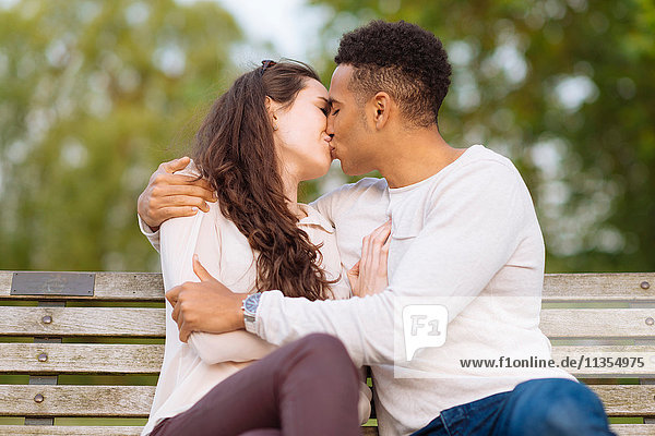 Junges Paar auf Parkbank küsst sich