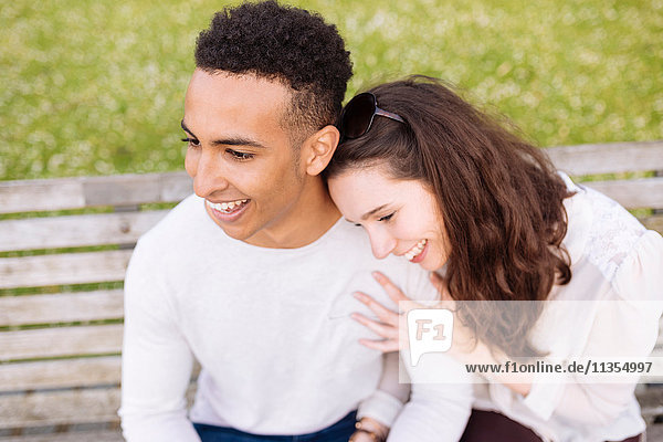 Hochwinkelaufnahme eines jungen Paares  das lächelnd auf einer Parkbank sitzt