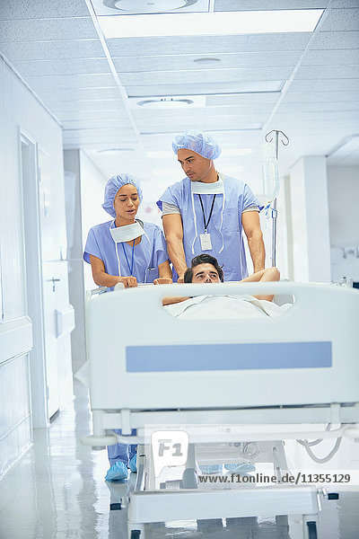 Ärzte in OP-Kleidung schieben Patient im Krankenhausbett