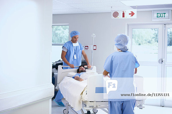 Ärzte in OP-Kleidung schieben Patient auf Krankenhausbett