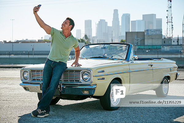 Man leaning against convertible car taking selfie  Los Angeles  California  USA