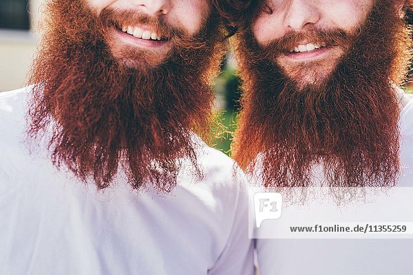 Beschnittenes Porträt junger männlicher Hipster-Zwillinge mit roten Bärten und weißen T-Shirts