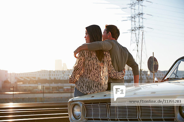 Couple leaning against car bonnet looking away  Los Angeles  California  USA
