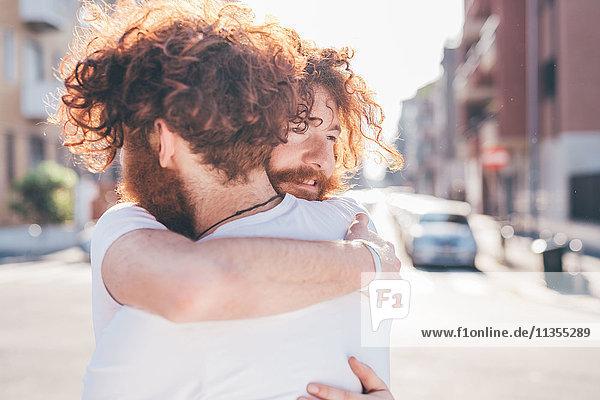 Junge männliche Hipster-Zwillinge mit roten Haaren und Bärten  die sich auf der Stadtstraße umarmen.