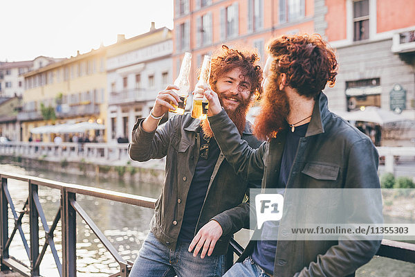 Young male hipster twins with red hair and beards making a toast on canal waterfront