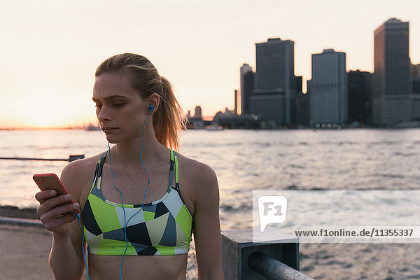 Junge Frau am Wasser die ein Smartphone benutzt Brooklyn New York USA