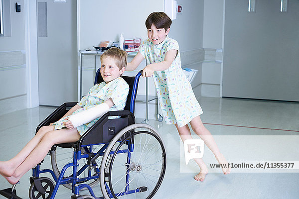 Boy patients pushing friend in wheelchair on hospital children's ward