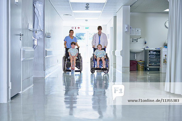 Sanitäter schieben Jungen-Patienten im Rollstuhl auf der Kinderstation eines Krankenhauses