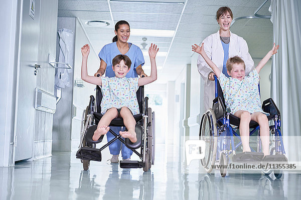 Sanitäter haben Spaß beim Schieben von Patienten im Rollstuhl auf der Kinderstation des Krankenhauses