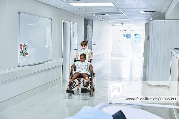 Junge Patienten schieben Freundin im Rollstuhl auf der Kinderstation des Krankenhauses