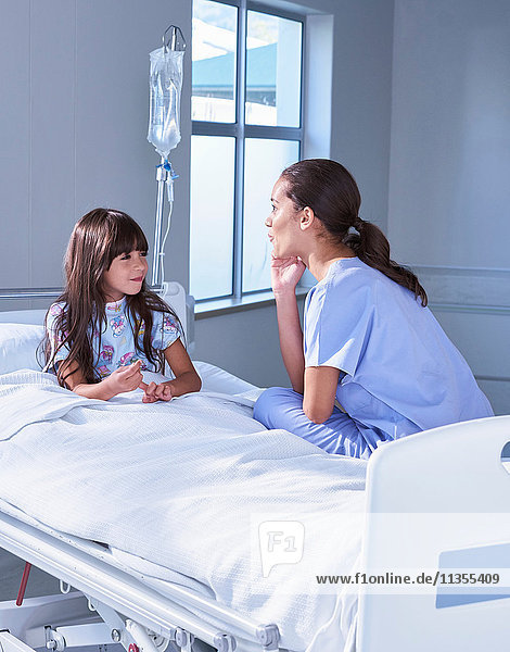 Krankenschwester im Gespräch mit einer Patientin  die auf der Kinderstation des Krankenhauses im Bett sitzt