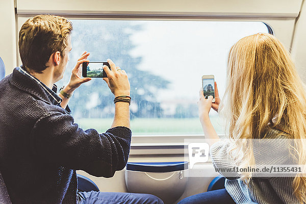 Young couple taking smartphone photographs through train carriage window  Italy