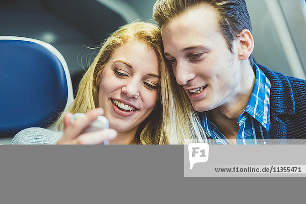 Young couple reading smartphone texts in train carriage