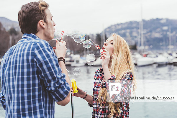 Young couple on waterfront blowing bubbles at each other  Lake Como  Italy