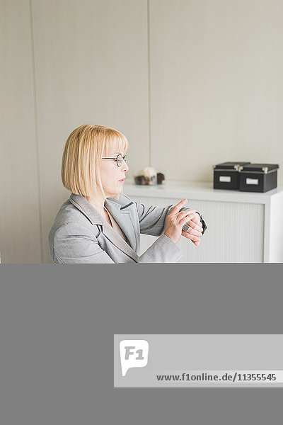 Reife Geschäftsfrau auf dem Schreibtisch mit Blick auf die Armbanduhr