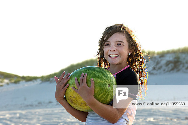 Porträt eines jungen Mädchens am Strand  das eine Melone hält und lächelt
