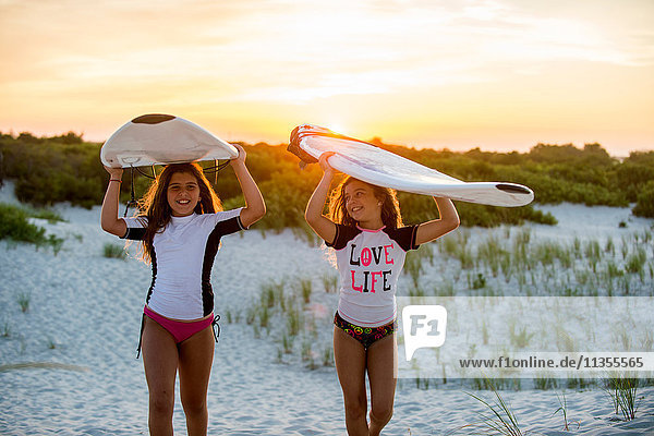 Zwei junge Mädchen am Strand  die Surfbretter tragen