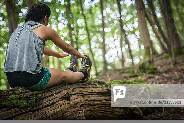 Mittlere erwachsene Frau  die im Wald trainiert  auf einem Baumstamm sitzt und sich streckt