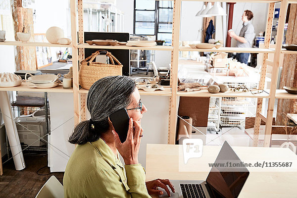 Woman in workshop using phone and laptop