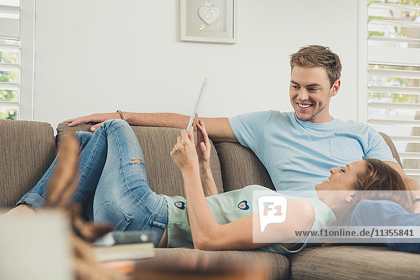 Couple relaxing on sofa using digital tablet smiling