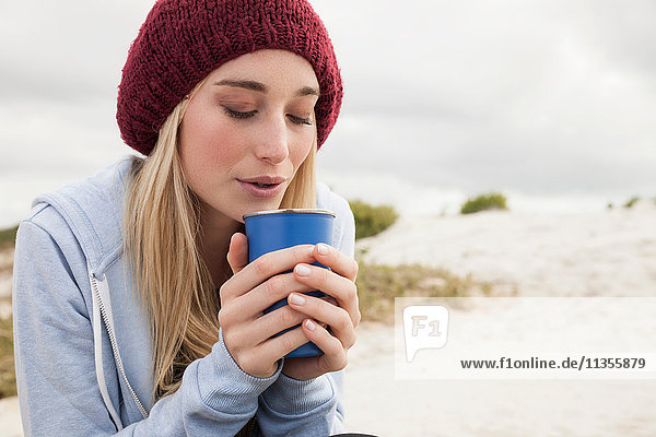 Junge Frau bläst an kaltem Tag in eine Tasse Kaffee