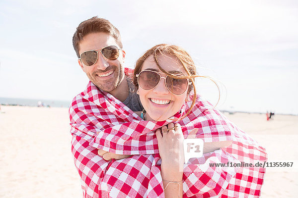 In eine Picknickdecke gewickeltes Paar schaut lächelnd in die Kamera  Coney Island  Brooklyn  New York  USA