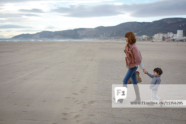 Mutter und Tochter halten am Strand Händchen