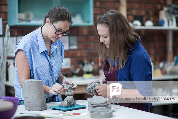 Two female potters shaping clay on workbench in workshop