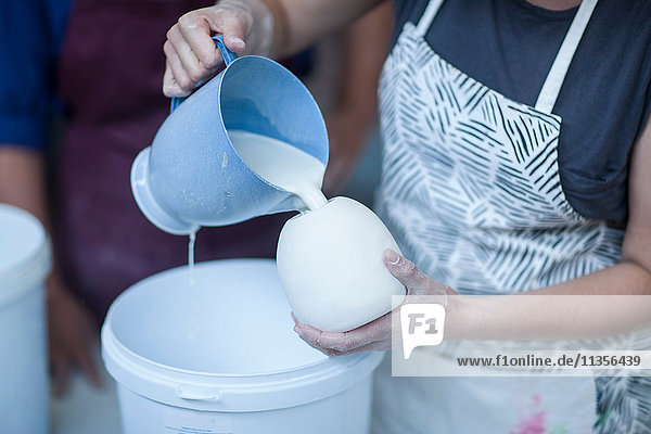 Female potter pouring ceramic glaze into vase in workshop