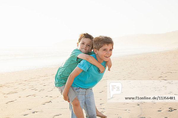 Junge gibt Bruder Huckepack am Strand