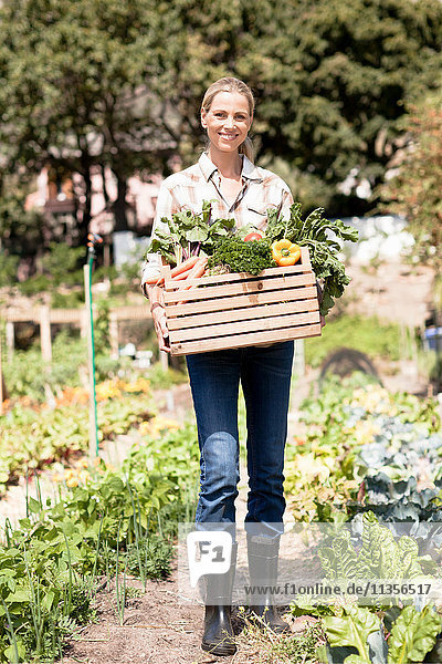 Porträt einer reifen Frau im Garten  die eine Kiste mit frischem Gemüse hält