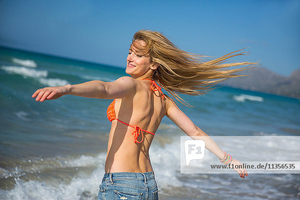 Junge Frau am Strand  Arme ausgestreckt  lächelnd