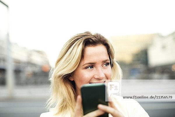 Glückliche junge Frau mit Handy in der Stadt gegen den klaren Himmel