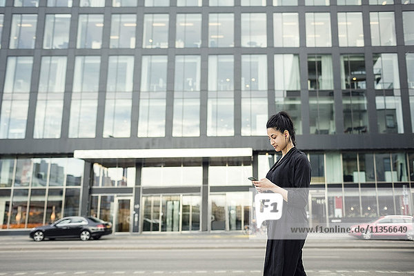 Junge Frau mit Handy gegen Bauen in der Stadt